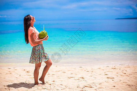 白热带海滩上带椰子鸡尾酒的年轻女子图片