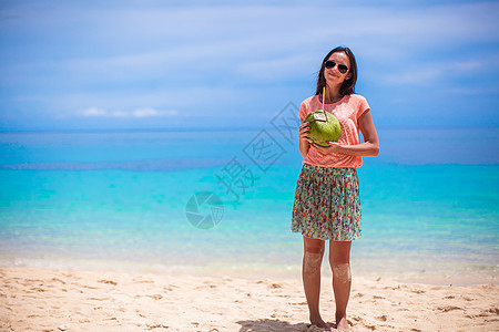 热带海滩上带椰子的可爱年轻女子图片