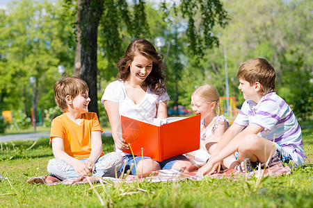 教师读书给夏季公园的孩子看书女性男孩们幼儿园友谊说谎教育童年婴儿女孩乐趣图片