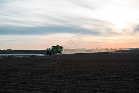 配备拖车的现代拖拉机农村机械收成农业农田灰尘天空土地牵引车日落图片