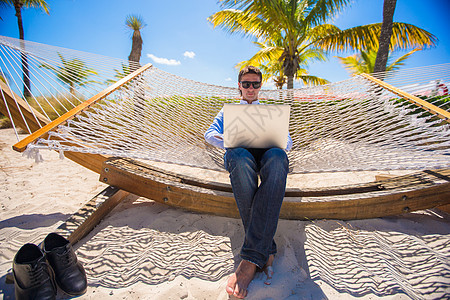 在暑假期间使用笔记本电脑坐在吊床上的商务人士图片