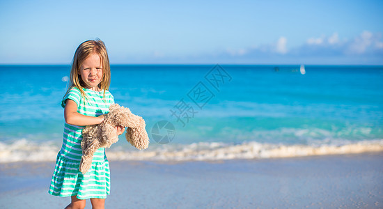 在热带海滩度假时 带着小兔子玩具的可爱的小姑娘假期旅游海岸海洋海岸线裙子异国支撑女士闲暇图片