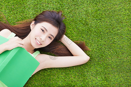 微笑的女学生 躺在草地上 藏着书籍公园绿地成人女孩享受幸福闲暇学习女性说谎图片