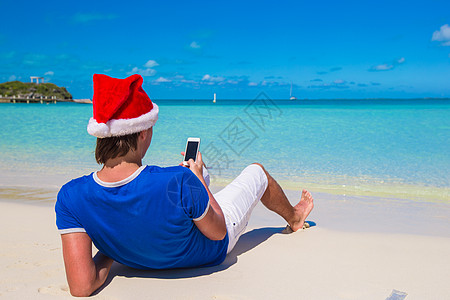 在热带卡利比海滩上挂着电话的圣塔帽青年男子背影手机海滩消息帽子地平线海滨闲暇假期男人太阳图片