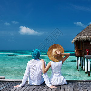 马尔代夫海滩码头的一对夫妇棕褐色女士幸福蜜月男人闲暇酒店太阳帽享受海洋图片