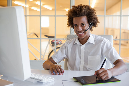 办公桌上使用数码器和耳机的临时性青年商务人士客户黑发混血快乐微笑工作男性键盘商务操作员图片