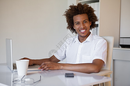 临时商务人士在桌子上对着相机微笑黑发男性商业休闲混血笔记本男人热饮电脑咖啡图片