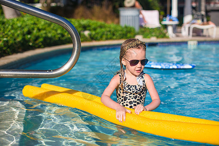 可爱的小女孩在游泳池玩得开心蓝色旅行牙齿水池娱乐童年喜悦游泳衣乐趣太阳镜图片