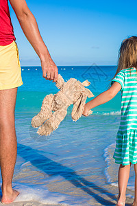 贴近小兔子玩具 在小女孩和爸爸的手中 海背景的父亲热带假期支撑海滩海岸父母旅游太阳女孩享受图片