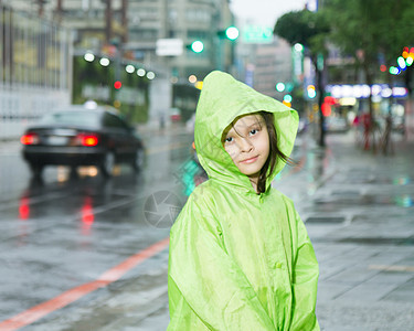 穿着绿色雨衣站在雨中年轻女孩微笑眼睛乐趣树木倾盆大雨外套下雨女性季节天气图片