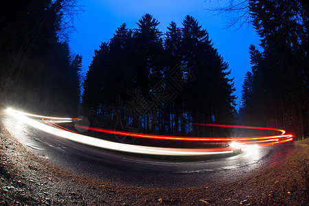在黄昏的森林道路上 快速穿越一条曲线的汽车图片