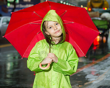 年轻女孩站在雨雨中 穿着雨衣和雨伞树木下雨倾盆大雨微笑天气外套乐趣孩子街道季节图片