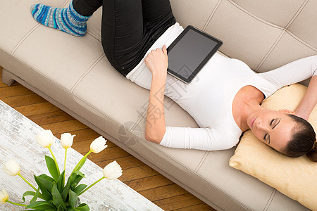 在沙发上使用 Tablet PC 的年轻女性网络屏幕公寓电脑长椅学生药片客厅黑发房间图片