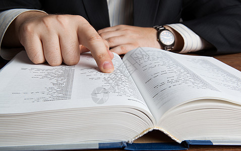 男人在大字典中寻找桌子报纸阅读商业计算器手指词本词汇表手表工作图片
