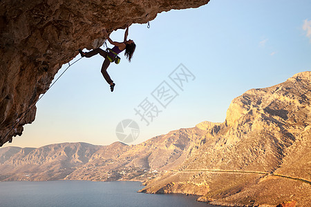 女孩在悬崖上攀岩的年轻女性月光运动高度天空岩石绳索斗争挑战女士登山者活动图片
