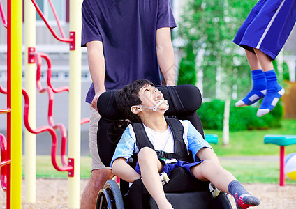 坐在轮椅上的残疾男孩 享受看朋友在平处玩耍需求机动性友谊社会操场公园朋友们孩子们孩子少数民族图片