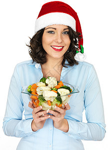Santa Hat持有碗煮熟混合蔬菜的年轻妇女晚餐厨师女性庆典女孩午餐女士家庭主妇吃饭成人图片