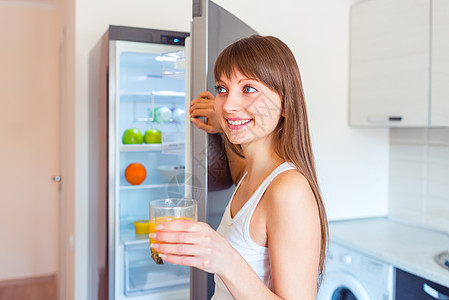 小黑发姑娘 冰箱旁边有一杯果汁的酒喜悦女性早餐女士微笑橙子女孩黑发日光图片