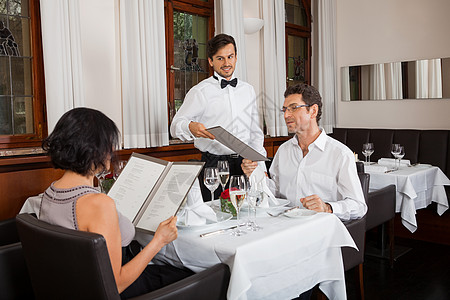 高档菜单餐馆里微笑的年轻夫妇食物俱乐部奢华餐厅桌子男人订购美食娱乐玻璃背景
