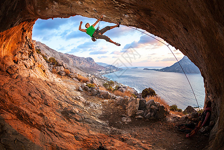 男性攀岩者在山洞的屋顶上攀爬悬崖登山者绳索成人天空洞穴运动岩石太阳日落图片