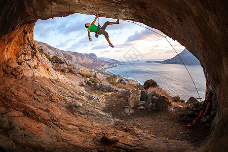 男性攀岩者在山洞的屋顶上攀爬成人男人风景太阳洞穴悬崖运动岩石登山者天空图片