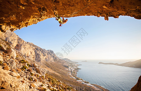 男性攀岩者在山洞的屋顶上攀爬悬崖登山者日落洞穴高度岩石成人风景天空太阳图片