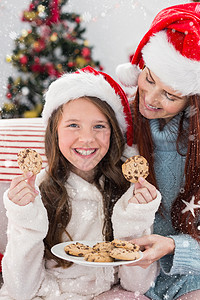 圣诞节美食喜庆母亲和女儿在沙发上带饼干的复合形象假期公寓下雪快乐住所女性客厅长椅家庭生活孩子背景