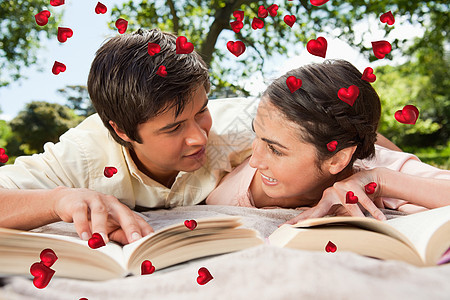 两个朋友在阅读毯子上的书时互相看对方的复合形象男人女性公园图书晴天喜悦夫妻头发男性女士背景图片