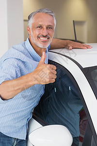 微笑的男人抱着一辆白色的车 举起拇指男性汽车购物拥抱运输快乐顾客代理商手势零售图片
