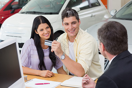 持有信用卡买车的一对微笑的夫妇运输男人销售营业员职业女士桌子代理商购物金融图片
