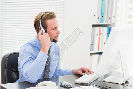 商务人士在用耳机说话时打电脑键字图片