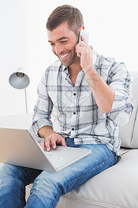 在家用笔记本电脑打电话时微笑的男人客厅呼唤沙发讨论电话技术长椅男性住所沟通图片