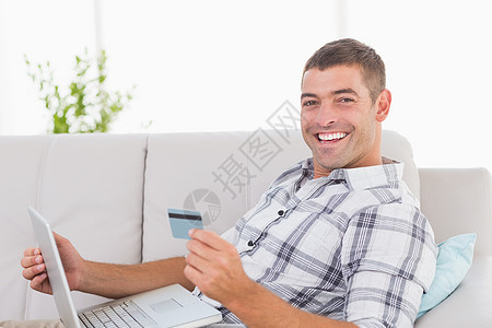 快乐的男人用信用卡通过笔记本电脑在网上购物图片