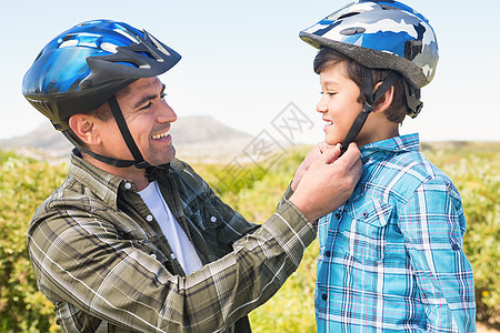 父亲戴着他儿子骑自行车的头盔闲暇农村男性活动感情阳光冒险家娱乐孩子晴天图片