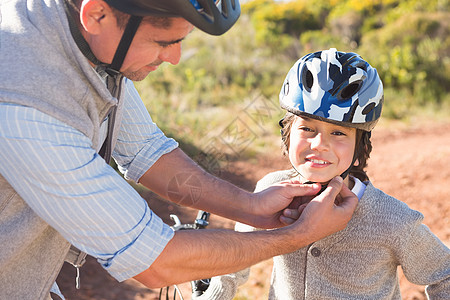 父亲在儿子头盔上剪皮快乐踪迹风景微笑孩子自行车晴天冒险家男生环境图片