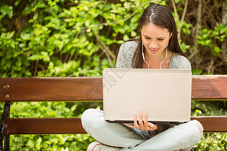 坐在长椅上听音乐和使用笔记本电脑的微笑学生高等教育音乐享受学习技术大学生耳机修订女性混血图片