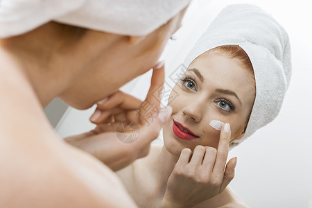 淋浴后的妇女应用奶油在她脸上毛巾化妆品卫生头发镜子洗漱温泉用品脸颊反射图片