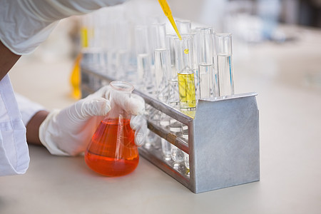 科学家在试验管中浇灌橙色液体手套药品化学家检查技术学习医疗保健实验室女士图片