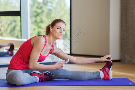 微笑着的女人 在健身房的垫子上伸展细胞训练技术青少年瑜伽女性女孩运动装播放耳机图片