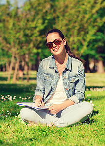 带着笔记本写作在公园的年轻微笑女孩牛仔布知识头发学校学习工作簿色调教育太阳镜铅笔图片