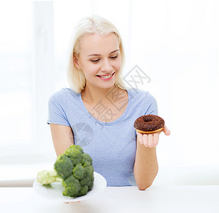 家里带着西兰花和甜甜圈的笑着女人饮食减肥蔬菜青少年沙拉生物损失营养女孩重量图片