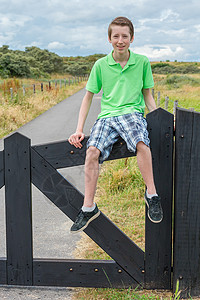 坐在天然黑色木栅栏上的荷兰十几岁的男孩图片