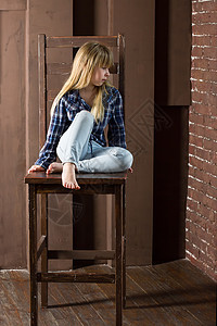 6岁女孩穿着牛仔裤和一件蓝衬衫坐在高椅子上图片