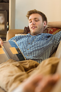 在沙发上、看书年轻人在沙发上读书男人房子住所长椅阅读休闲家庭客厅快乐说谎背景