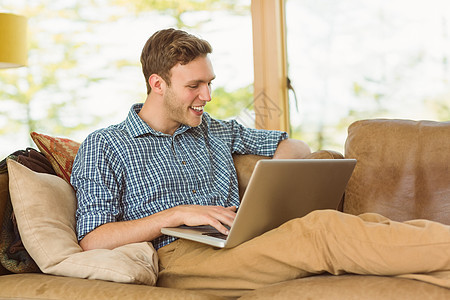 年轻人用笔记本电脑在沙发上放松快乐休闲技术长椅男性男人格纹客厅衬衫公寓图片