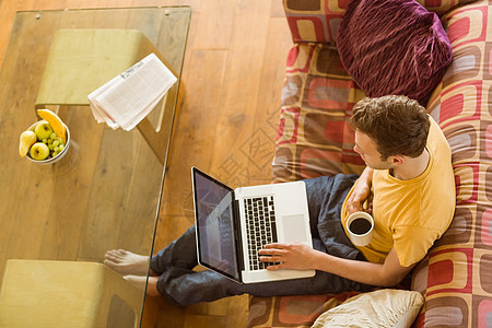 年轻人在沙发上用笔记本电脑服装公寓客厅热饮家庭休闲技术微笑住所男性图片