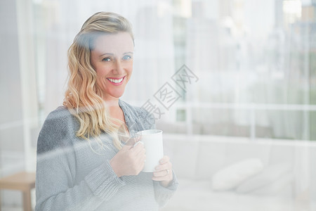喝着咖啡的金发美女微笑女士休闲服装家庭生活金发女郎窗户家庭住所公寓房子图片