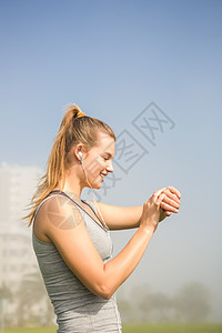 利用聪明手表微笑运动的金发美女公园身体女性快乐运动服技术阳光耳机晴天调子图片