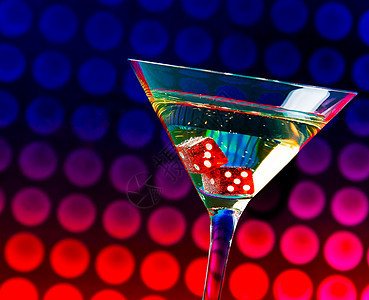 鸡尾酒杯中的红色骰子 在多色梯度bokeh上背景图片