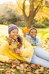 年轻母亲和儿子坐在树叶上保暖女士说谎草原衣服公园绿地衣物童年快乐图片